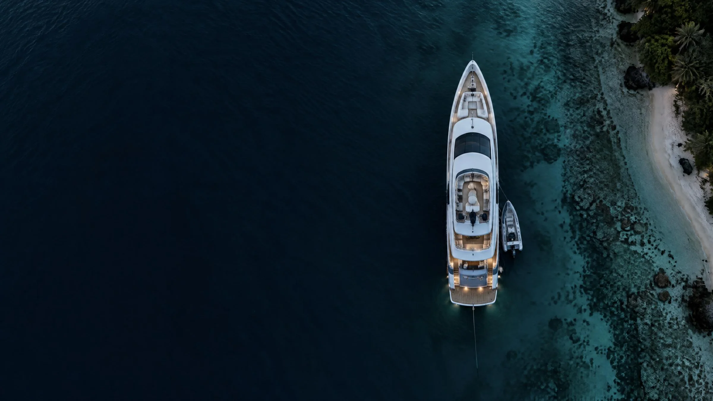 Aerial view of a superyacht moored beside a tropical reef at dusk