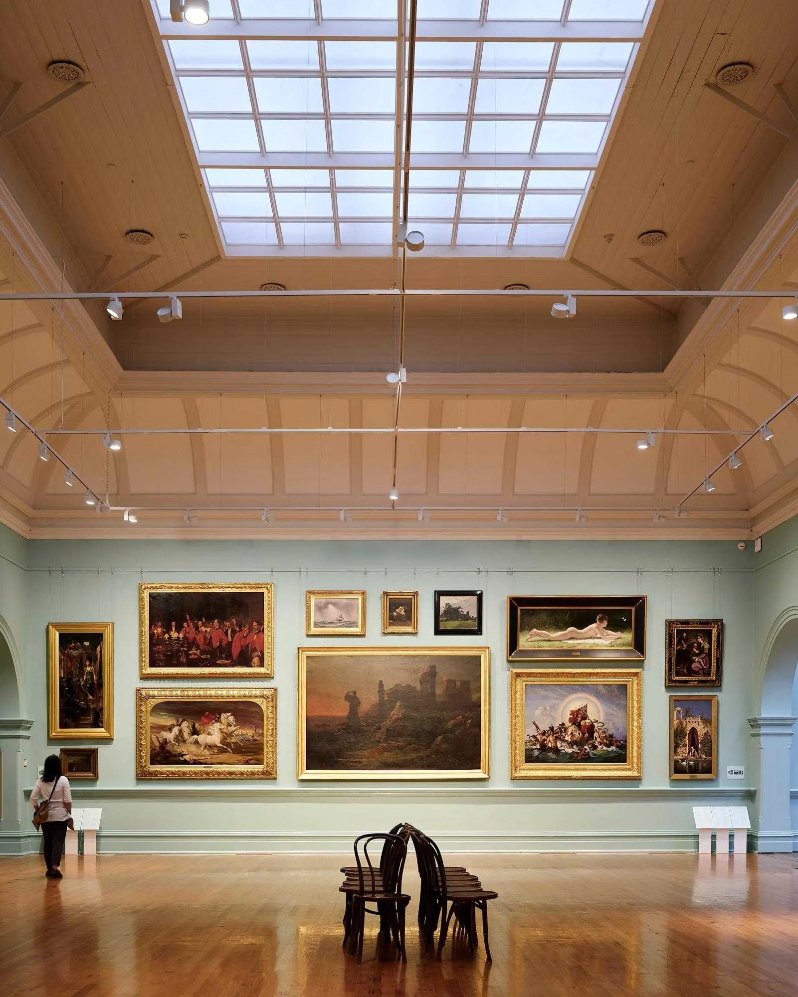 A gallery hung with gilt-framed paintings beneath a skylight