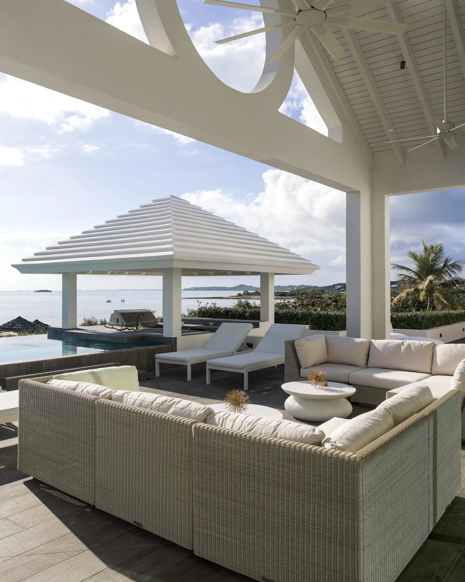A covered terrace with lounge seating beside an infinity pool overlooking the sea